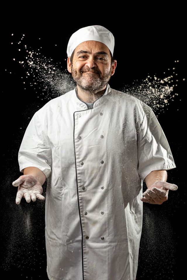 Chef lançant de la farine, souriant, sur fond noir