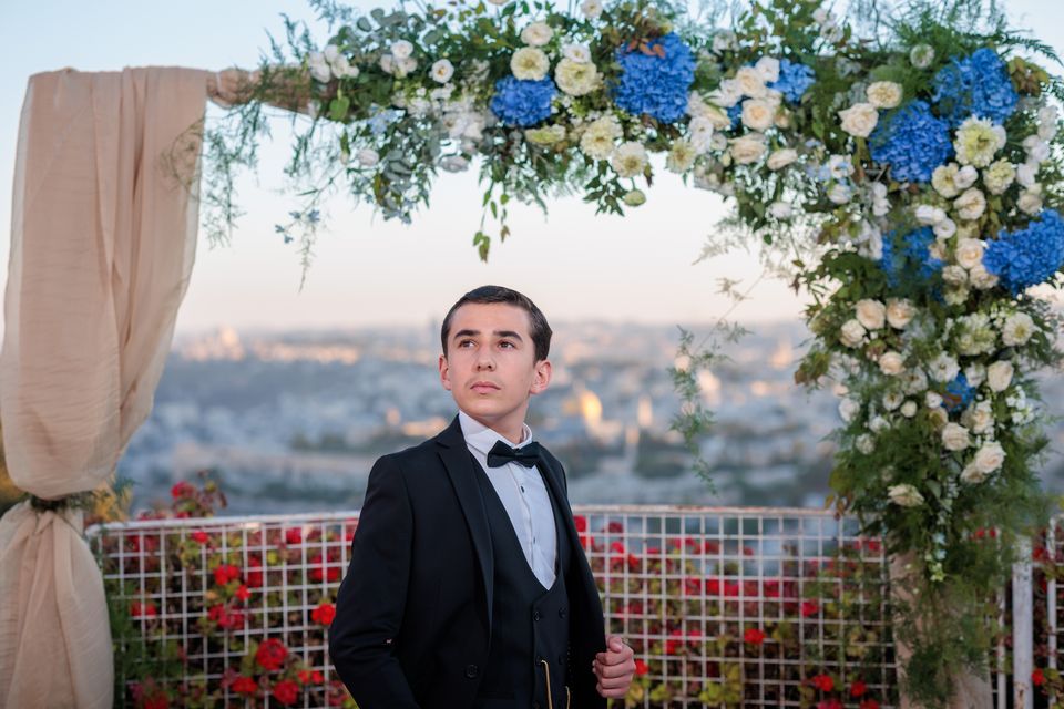 Garçon en smoking sous une arche de fleurs, la ville de Jerusalem en arrière-plan