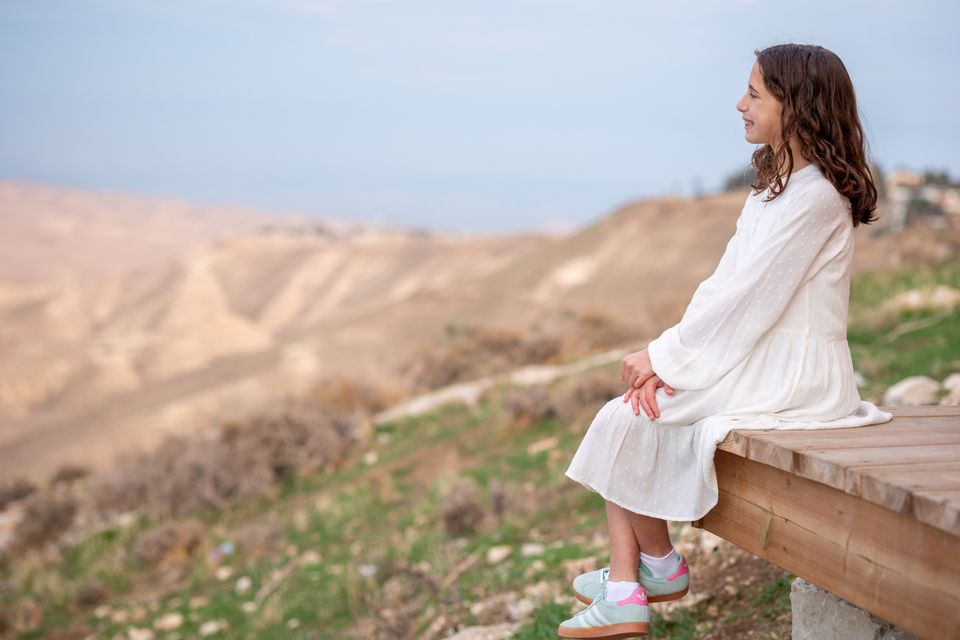 Jeune fille en robe blanche assise face aux collines du désert de Judée