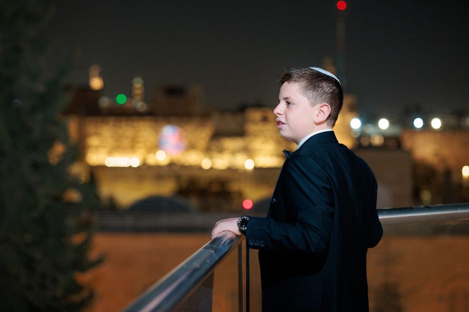 Garçon de bar mitsva en costume et kippa, la nuit, face aux lumières de la vieille ville de Jerusalem