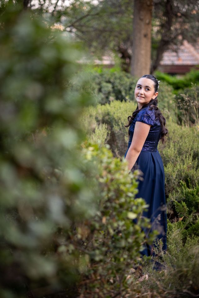 Jeune fille en robe bleu nuit à paillettes, souriante au milieu des buissons