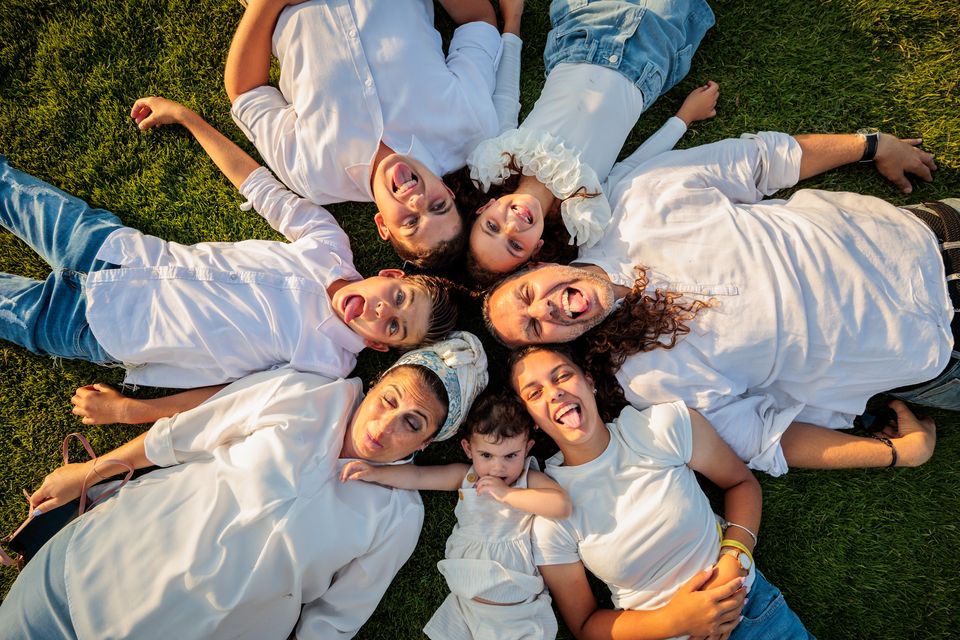 Famille allongée en cercle sur l'herbe, têtes rapprochées, qui fait des grimaces