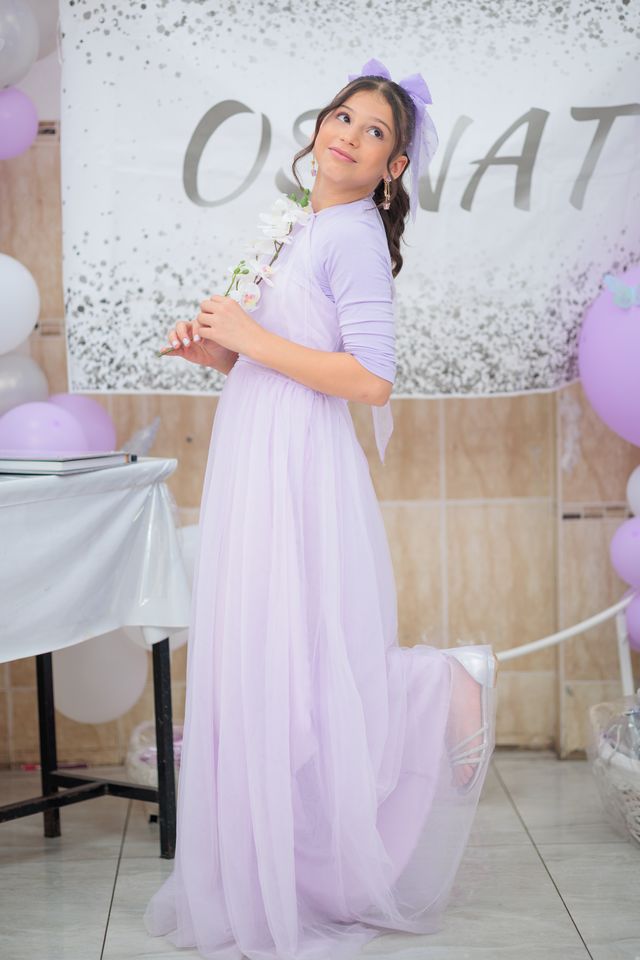 Jeune fille en robe de tulle mauve, une fleur à la main, le jour de sa bat mitsva
