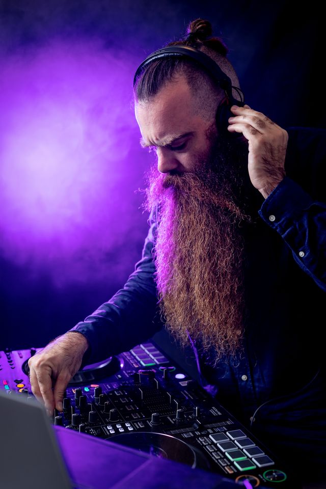 DJ barbu au casque derrière ses platines, sous une lumière violette