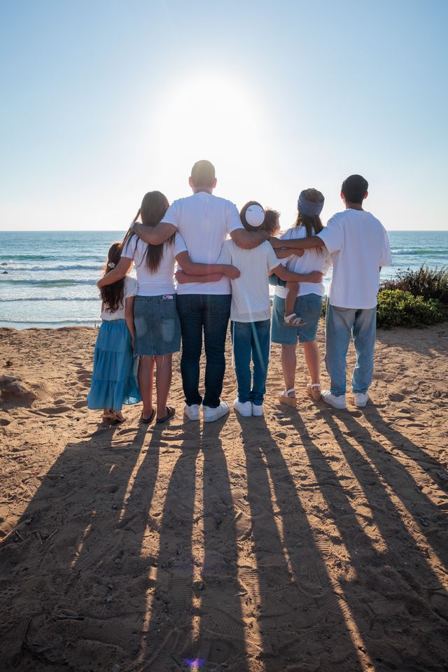Famille bras dessus bras dessous sur la plage, face à la mer, vue de dos