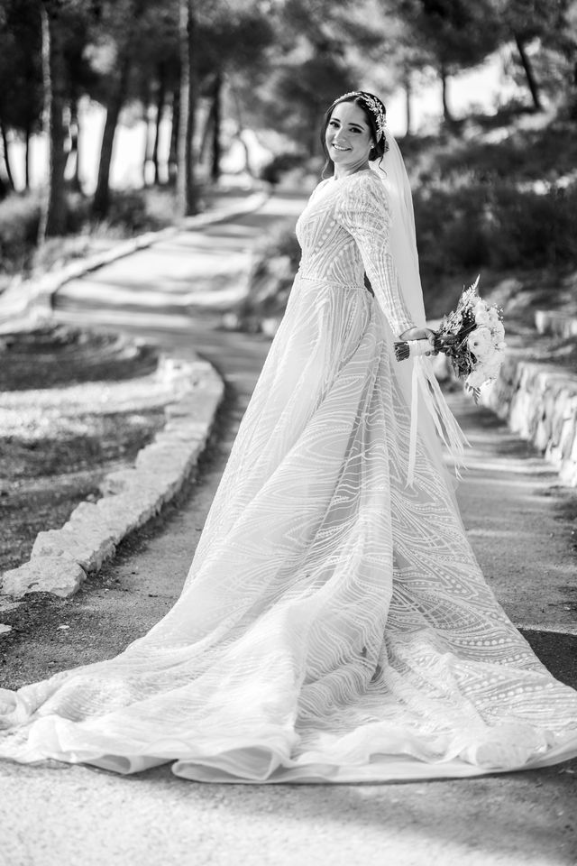 Mariée en noir et blanc, sa longue traîne sur un chemin bordé de pins