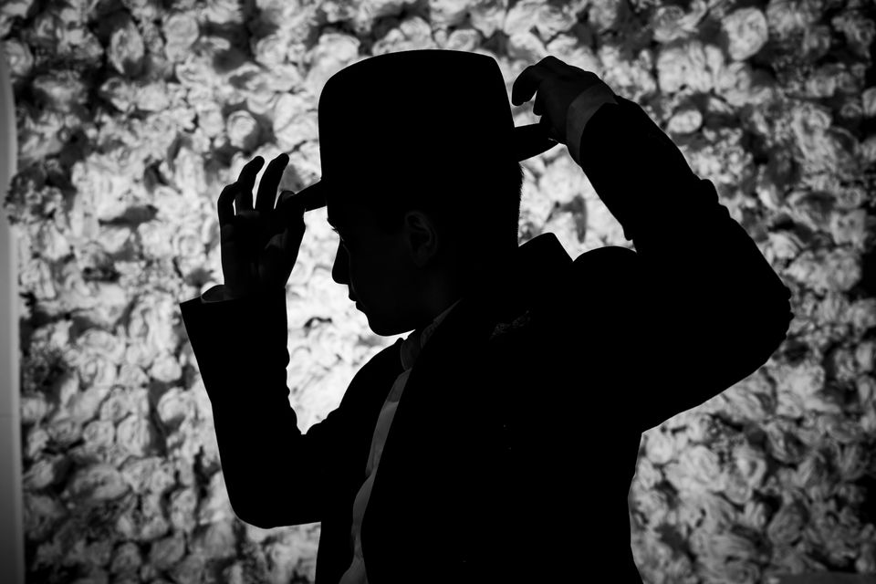 Silhouette d'un garçon qui ajuste son chapeau noir, devant un mur de fleurs